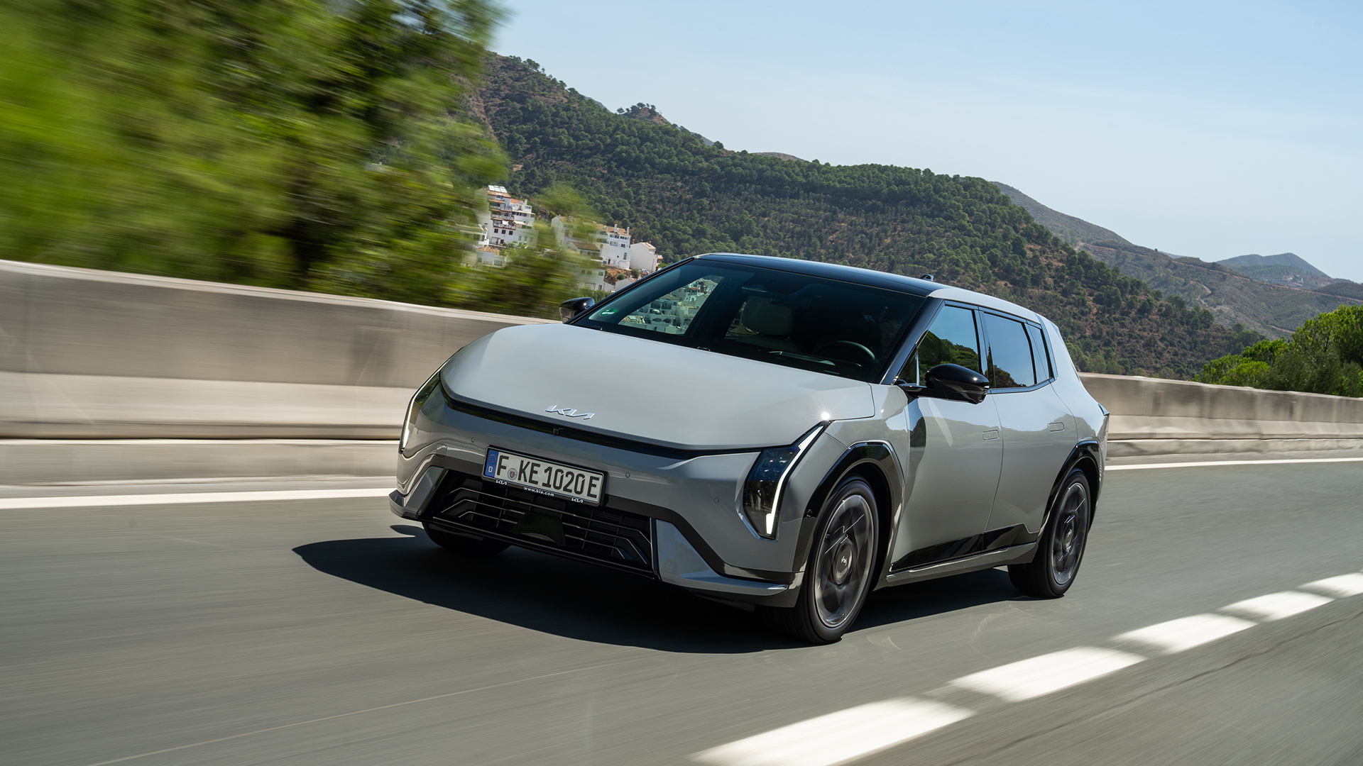 Kia EV4: Siva električna Kia EV4 tijekom dinamične vožnje planinskom cestom, s brdovitim krajolikom u pozadini