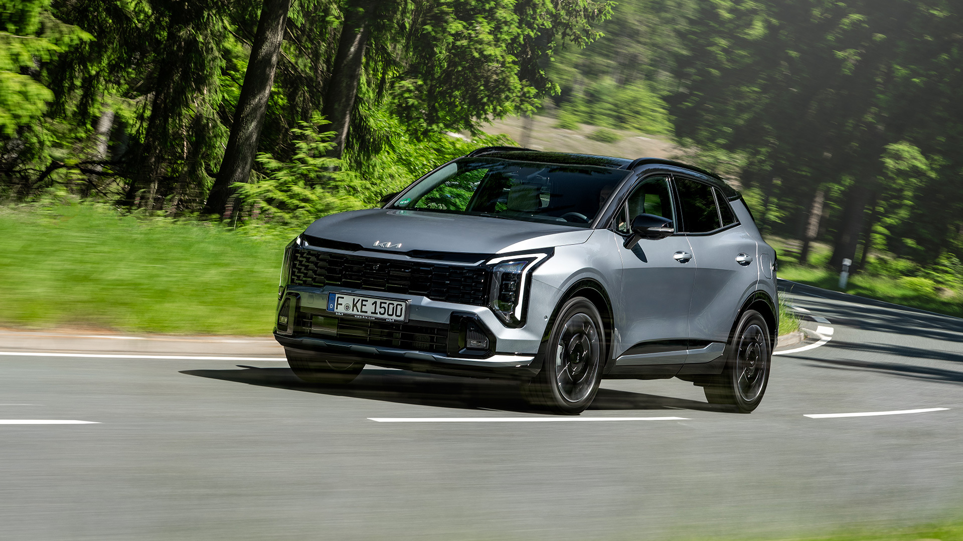 Kia Sportage: Siva Kia Sportage tijekom dinamične vožnje zavojitom cestom kroz zelenu šumu