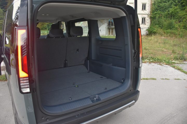 Temno zelena električna Kia PV5 Passenger, parkirana v naravnem okolju - poudarek na prostornem prtljažniku