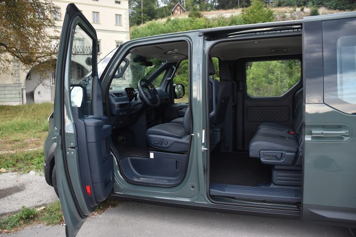 Temno zelena električna Kia PV5 Passenger, parkirana v naravnem okolju - poudarek na prostorni kabini in velikih vratih