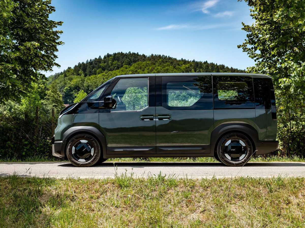 Kia PV5 Passenger v temno zeleni barvi, bočni pogled na vozilo v naravnem okolju.