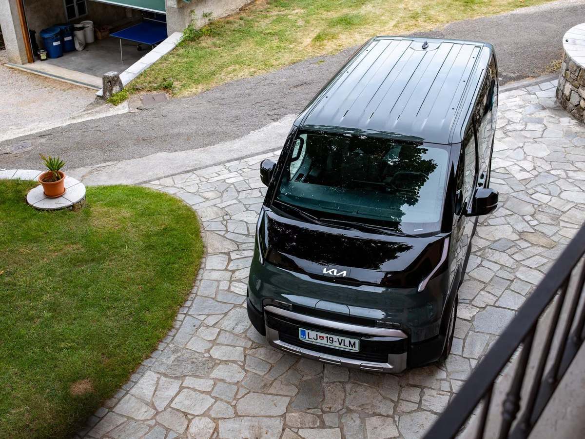 Temno zeleni električni Kia PV5 Passenger, fotografiran od zgoraj na tlakovanem dvorišču.