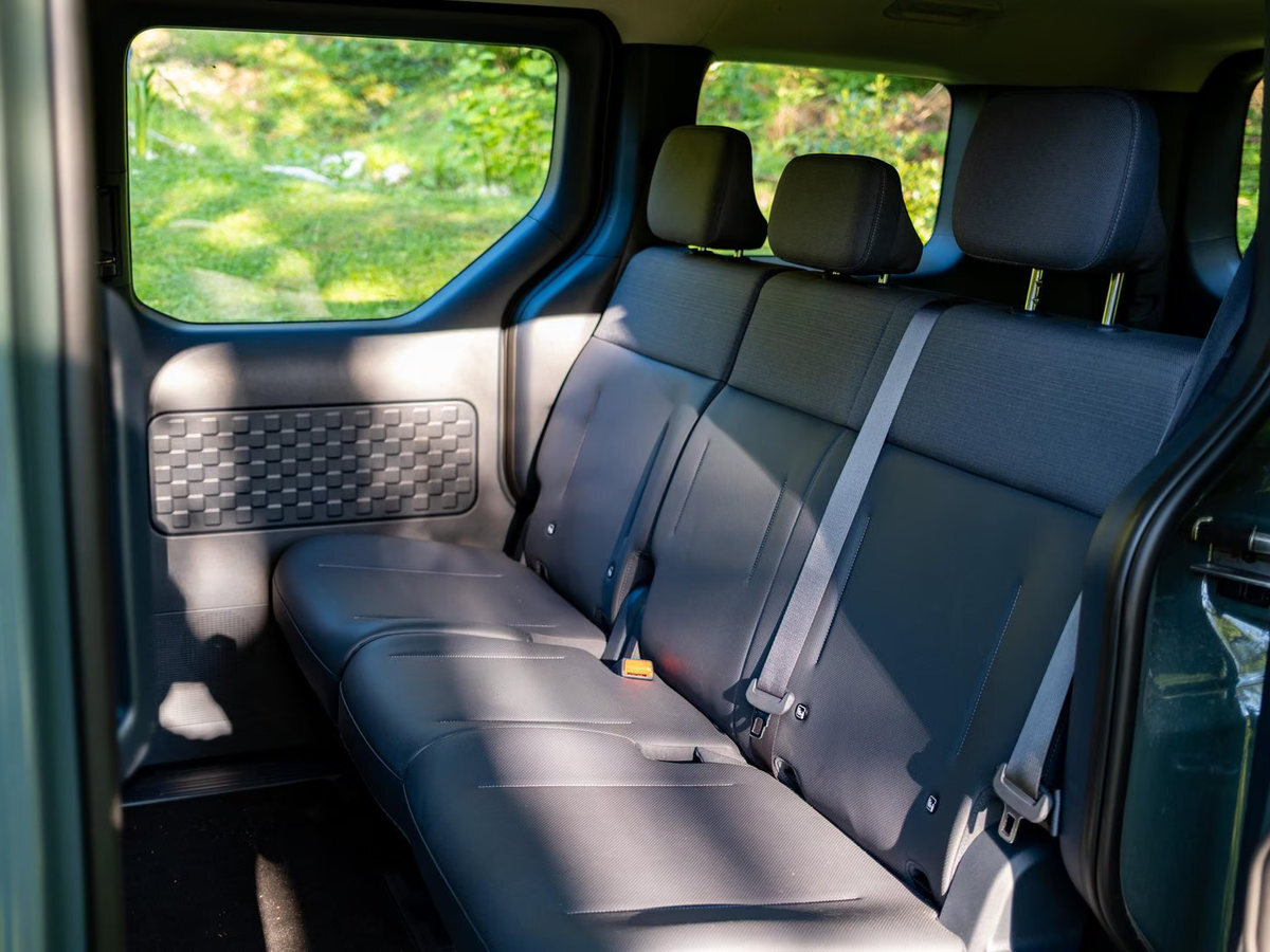 Zadnja sedežna klop modela Kia PV5 Passenger s tremi vzglavniki in varnostnimi pasovi.
