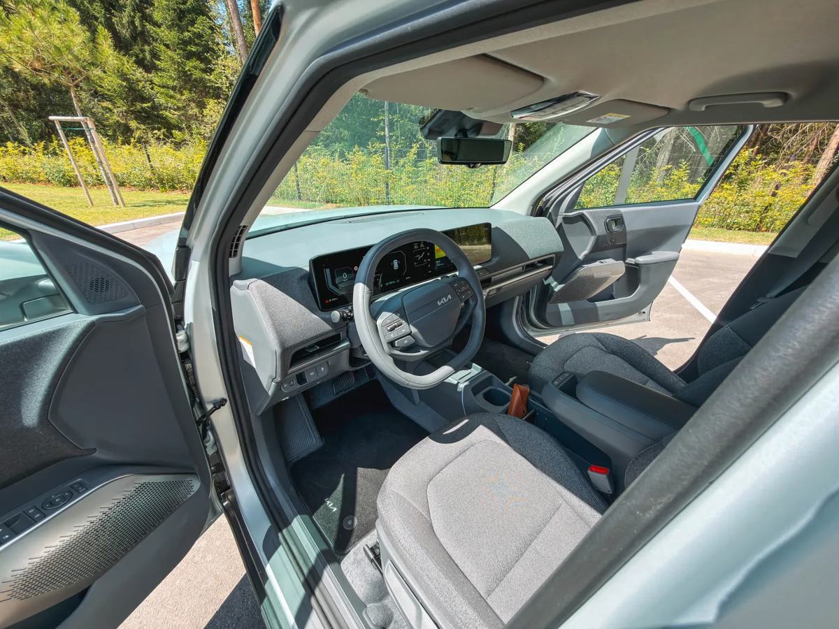 Pogled v potniško kabino modela Kia EV2 z armaturno ploščo, digitalnimi zasloni in sprednjima sedežema.